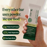 Hand holding a lemon coconut protein bar with product details on a blurred background - view 2